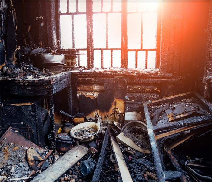 a fire damaged kitchen with debris littering the floor and soot covering everything