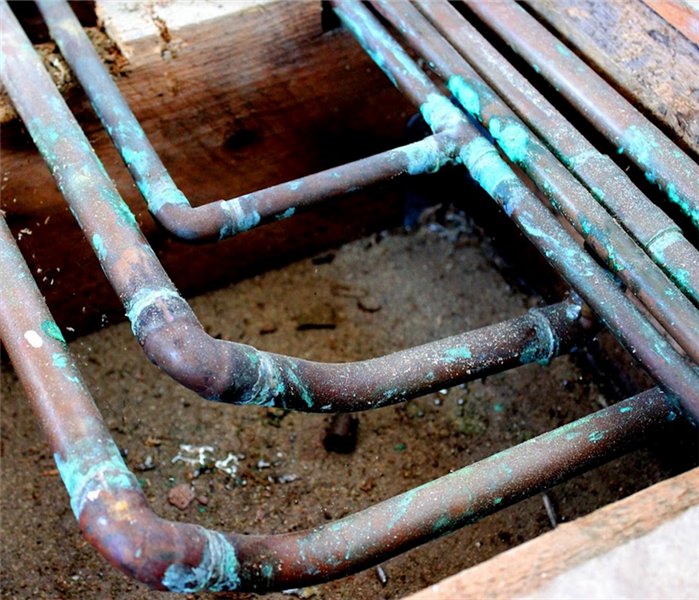 copper pipes covered in rust under the floor of a house